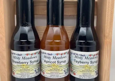 Strawberry, apricot, and tayberry syrup bottles in a wood crate